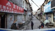 This photo taken on February 23, 2020 shows people standing on a street by a barrier to stop others from entering, in Wuhan in China's central Hubei province. / AFP / STR