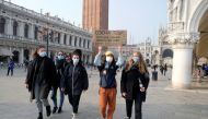 People wear protective face masks as they walk in St. Mark's square holding a placard that reads 