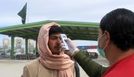 A health worker takes the temperature of a man, who returned from Afghanistan, for a medical observation as a preventive measure following the coronavirus outbreak, outside a medical camp set up near the Friendship Gate, crossing point at the Pakistan-Afg