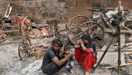 A woman sitting with her husband and their child reacts next to damaged property after their house was burnt by a mob on Tuesday in a riot affected area after clashes erupted between people demonstrating for and against a new citizenship law in New Delhi,