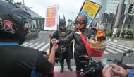 People wearing characters clothes of local hero Gundala (R) and Batman (L) offer Indonesian traditional herbal drinks “Jamu” to motorists as they encourage them to stay healthy and fight COVID-19 in Solo on March 4, 2020. / AFP / ANWAR MUSTAFA 