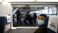 A mask-clad passenger looks on from his seat as others (background) alight from their train at the railway station in Wuhan, China's central Hubei province on March 10, 2020./ AFP / Noel Celis