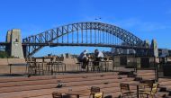 An elderly couple sit at a table in front of the Sydney Harbour Bridge, following an outbreak of coronavirus (COVID-19), in Sydney, Australia, on March 19, 2020. (Steven Saphore - Anadolu Agency)