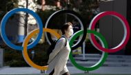 FILE PHOTO: A woman wearing a protective face mask, following an outbreak of the coronavirus disease (COVID-19), walks past the Olympic rings in front of the Japan Olympics Museum in Tokyo, Japan March 13, 2020. REUTERS/Athit Perawongmetha