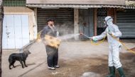 A Moroccan health ministry worker disinfects a man walking a dog and carrying a mat in the capital Rabat on March 22, 2020. AFP / Fadel Senna
 