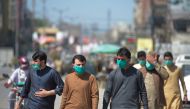 People wearing facemask walks along a road of a closed market area in Rawalpindi on March 22, 2020, after Punjab Province government announced the closing of shops and markets amid concerns over the spread of the COVID-19 novel coronavirus.   / AFP / Faro