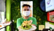 Pizza Home restaurant owner Hoang Tung poses with a coronavirus-themed burger in Hanoi on March 26, 2020, amid restrictions being put in place to contain the spread of the COVID-19 coronavirus. / AFP / Manan Vatsyayana 
