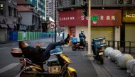 Delivery men wwearing a wearing a facemask as a preventive measure against the COVID-19 coronavirus wait for mobile orders along a street in Wuhan, in China's central Hubei province on April 1, 2020. / AFP / NOEL CELIS