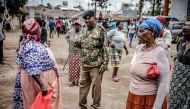 A Kenyan Police officer explains the physical distancing measures that have to be followed to a group of people affected by the measures adopted by the Kenyan Government to stop the spread of COVID-19 coronavirus while they wait for boxes with food and ot