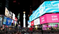 People walk in Times Square, Manhattan while some screens are seen illuminated in blue as part of the 