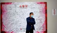 A man wearing a face mask stands in front of a tarpaulin filled with signatures and messages at the Leishenshan Hospital that had offered beds for coronavirus patients in Wuhan, in China’s central Hubei province on April 11, 2020. / AFP / Noel Celis