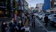 A group of people wearing face masks amid concerns over the COVID-19 novel coronavirus walk along a street in Seoul on April 12, 2020. / AFP / Ed JONES
