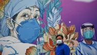 TOPSHOT - A man wearing a face mask walks in front of a mural at the Leishenshan Hospital that had offered beds for coronavirus patients in Wuhan, in China’s central Hubei province on April 11, 2020. / AFP / Noel Celis