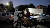 A health worker uses an infrared thermometer to measure the temperature of a motorcyclist on a road during a nationwide lockdown to slow the spreading of the coronavirus disease (COVID-19) in Ahmedabad, India, April 27, 2020. REUTERS/Amit Dave