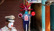 A police officer wearing a protective face mask walks past a novel coronavirus-themed scarecrow cutout put up in a residential area during an extended lockdown to slow the spreading ofthe coronavirus disease (COVID-19) in the old quarters of Delhi, India,