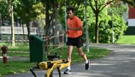 (FILES) In this file photo taken on May 8, 2020, a man jogs past a four-legged robot called Spot, which broadcasts a recorded message reminding people to observe safe distancing as a preventive measure against the spread of the COVID-19 coronavirus, durin