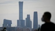 A man wearing a face mask looks at the skyline of the central business district (CBD) from a park in Beijing on May 23, 2020. / AFP / WANG ZHAO