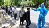 A volunteer wearing a protective suit checks the body temperature of homeless people standing in queue to get free lunch packets on the roadside after the goverment eased a nationwide lockdown as a preventive measure against the COVID-19 coronavirus, in N