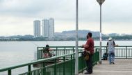 People fish from a jetty at a seafront in Singapore across Malaysia's southern state of Johor, seen in the background on June 23, 2020. / AFP / Roslan RAHMAN