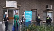 Police and medical workers stand outside an entrance to a public housing estate which is undergoing a forced lockdown in Melbourne on July 10, 2020, as the city records another 288 new cases in a fresh outbreak of the COVID-19 coronavirus.  AFP / William 