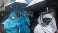A health worker in personal protective equipment (PPE) walks holding an umbrella on a rainy day during a check up campaign for the coronavirus disease (COVID-19) in Mumbai, India, July 14, 2020. REUTERS/Francis Mascarenhas
