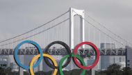 A large size Olympic rings symbol (W32.6m x H15.3m) is seen in front of Rainbow Bridge at Tokyo Waterfront in the waters of Odaiba Marine Park on August 6, 2020 before being transferred back to the factory where it was manufactured for a safety inspection