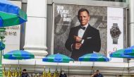 Security guards sit in the Erawan Shrine compound under an advertisement poster featuring Daniel Craig in the new James Bond movie 
