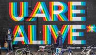 A pedestrian wearing a face mask or covering due to the COVID-19 pandemic, walks past a mural reading 