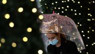A pedestrian wearing a face mask shelters under an umbrella as she passes a Christmas light display at a department store in central London on October 29, 2020. / AFP / JUSTIN TALLIS
