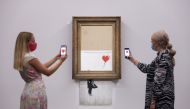 A gallery assistant poses by 'Love is in the Bin', an artwork by Banksy, which will be for sale in an auction, at Sotheby's in London, Britain, September 3, 2021. Reuters/Tom Nicholson