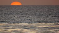 The sun sets as a fisherman casts his line in the Pacific Ocean while sitting on a surfboard off the coast of Cardiff, California April 1, 2008. REUTERS/Mike Blake/File Photo