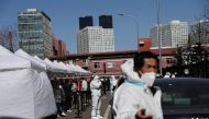 Workers in protective suits stand next to people lining up at a makeshift nucleic acid testing site during a mass testing for the coronavirus disease (COVID-19), in Chaoyang district of Beijing, China March 14, 2022. REUTERS/Tingshu Wang