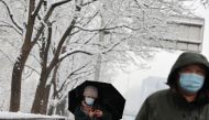 People wearing face masks to prevent the spread of the coronavirus disease (COVID-19), walk on the street amid snowfall in Beijing, China March 18, 2022. REUTERS/Tingshu Wang