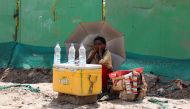  A girl selling water uses an umbrella to protect herself from the sun as she waits for customers on a hot summer day, in New Delhi, India, April 27, 2022. REUTERS/Anushree Fadnavis/File Photo