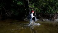 Andrew Otazo, who calls himself an amateur mangrove cleaner, walks on the shore as he removes trash from the mangroves at Crandon Park in Miami, Florida, US, July 13, 2022. (REUTERS/Marco Bello)