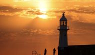 People stand on Mevagissey Harbour wall as the sun rises in Mevagissey Harbour in Cornwall, Britain, July 18, 2022. REUTERS/Tom Nicholson