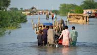 Men walk along a flooded road with their belongings, following rains and floods during the monsoon season in Sohbatpur, Pakistan, August 28, 2022. (REUTERS/Amer Hussain)