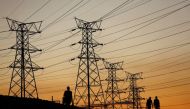 Locals walk past electricity pylons during frequent power outages from South African utility Eskom, caused by its aging coal-fired plants, in Soweto, South Africa, July 3, 2022. REUTERS/Siphiwe Sibeko//File Photo