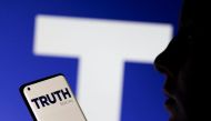 The Truth social network logo is seen displayed behind a woman holding a smartphone in this picture illustration taken on February 21, 2022. REUTERS/Dado Ruvic/Illustration
