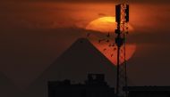 In this file photo taken on November 20, 2022, a flock of pigeons flies as the sun sets behind the Great Pyramid of Khufu and a cellular broadcast antenna tower in Giza, the twin city of Egypt's capital Cairo, on November 20, 2022. (Photo by Amir MAKAR / AFP)