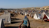 A displaced girl carries a bottle of water she filled from nearby stranded flood-waters, as her family takes refuge in a camp, in Sehwan, Pakistan, September 30, 2022. (REUTERS/Akhtar Soomro)