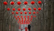 A woman and a child walk along a road with red lanterns hanging on trees for the upcoming Chinese Lunar New Year celebrations at a park in Beijing on January 11, 2023. (Photo by Wang Zhao / AFP)