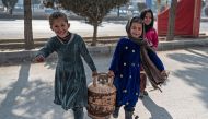 Afghan girls carry a gas cylinder along a street in Kabul on January 17, 2023. (Photo by Wakil Kohsar / AFP)