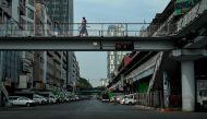 People walk past on a bridge an almost empty street during a 