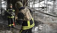 Ukrainian firefighters roll a fire hose as they work to put out fire in a shopping mall following a Russian shelling in Kherson, on February 3, 2023, amid the Russian invasion of Ukraine. (Photo by Genya SAVILOV / AFP)