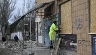 People clear debris and cover broken windows in shops damaged following strike in Kherson on February 4, 2023, amid Russian invasion of Ukraine. - Russian forces have been shelling the southern region of Kherson, after withdrawing its forces from the region's main city last year. (Photo by Genya SAVILOV / AFP)
