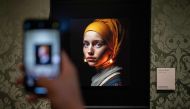 A visitor takes a picture with his mobile phone of an image designed with artificial intelligence by Berlin-based digital creator Julian van Dieken (C) inspired by Johannes Vermeer's painting 