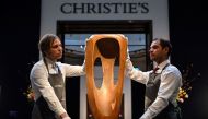 Two gallery assistants hold a sculpture by British artist Barbara Hepworth called 