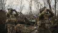 Ukrainian servicemen (L and R) look on with binoculars next to another (C) sitting on an anti-air gun near Bakhmut, on March 24, 2023. (Photo by Aris Messinis / AFP)
 