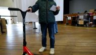 A person holds a ballot and an e-scooter during a municipal public 
